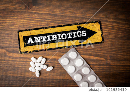 Antibiotics Concept. Yellow direction sign with arrow and text. Pills on a wooden background 101926459