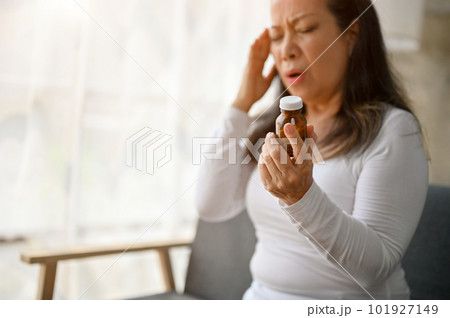 Unhealthy Asian senior mature woman holding her medicine bottle, suffering from headache Unhealthy Asian senior mature woman holding her medicine bottle, suffering from headache 101927149