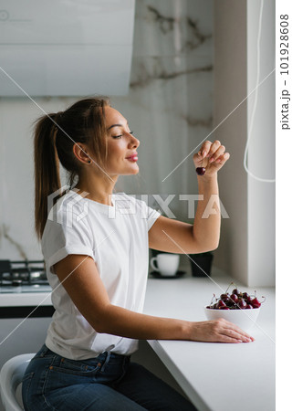 Young woman is eating a sweet cherry. Portrait of a beautiful girl with a cherry in the kitchen. Young woman is eating a sweet cherry. Portrait of a beautiful girl with a cherry in the kitchen. 101928608