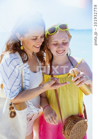 smiling mother and teenage daughter at beach using sunscreen 101932759