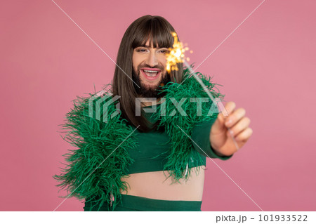 Delighted laughing transgender with makeup and wig wears green feather party dress holding sparkler Delighted laughing transgender with makeup and wig wears green feather party dress holding sparkler 101933522
