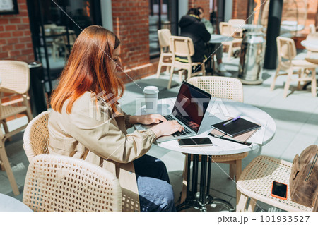 Young woman enjoying a coffee, 30s girl with laptop sitting on the cafe terrace on the modern city street. Traveler, Online education, urban, working or shopping concept Young woman enjoying a coffee, 30s girl with laptop sitting on the cafe terrace on the modern city street. Traveler, Online education, urban, working or shopping concept 101933527
