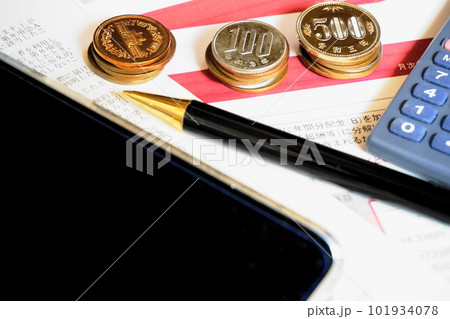 資料の上に並べられた各種硬貨と電卓、ペン、スマートフォン 101934078