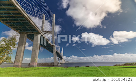 Vasco da Gama bridge timelapse hyperlapse with green lawn on a waterfront and blue cloudy sky. Lisbon, Portugal. 101934225