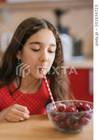 Teenage girl drinks juice from a cherry in a plate through a straw. The concept of an organic natural drink Teenage girl drinks juice from a cherry in a plate through a straw. The concept of an organic natural drink 101934723