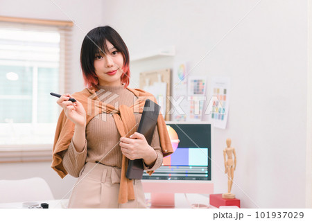 A portrait of a beautiful, professional, and confident millennial creative and stylish young female freelance designer hands holding a tablet and stylus pen while standing at her desk in office. 101937029