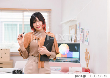A portrait of a beautiful, professional, and confident millennial creative and stylish young female freelance designer hands holding a tablet and stylus pen while standing at her desk in office. 101937030