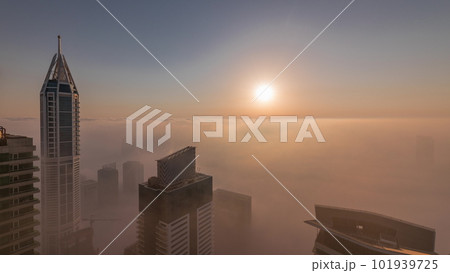 Rare early morning winter fog above the Dubai Marina skyline and skyscrapers lighted by sun aerial timelapse. 101939725