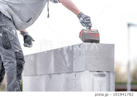 the mason applies glue to the concrete forms. construction of a wall of concrete bricks the mason applies glue to the concrete forms. construction of a wall of concrete bricks 101941762
