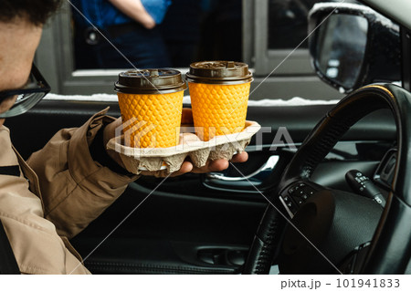 a man in a car holds cups of coffee that he ordered while driving or passing by. a man in a car holds cups of coffee that he ordered while driving or passing by. 101941833
