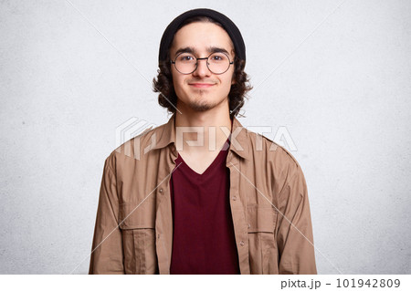 Close up portrait of good looking boy with curly hair, beard, wears round transparent glasses, models against white background. Copy space for your promotional text. People and lifestyle concept. 101942809