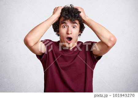 Close up portrait of astonished young man keeps hands on head, jaw dropped, hears terrible news from friend, expresses surprisement, isolated over pink studio wall. People, comunication concept. Close up portrait of astonished young man keeps hands on head, jaw dropped, hears terrible news from friend, expresses surprisement, isolated over pink studio wall. People, comunication concept. 101943270