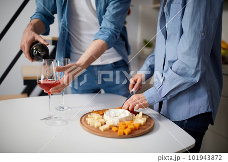 Romantic dinner preparation. Beautiful young couple celebrating holidays at home, wife cutting cheese, husband pouring red wine. Romantic dinner preparation. Beautiful young couple celebrating holidays at home, wife cutting cheese, husband pouring red wine. 101943872