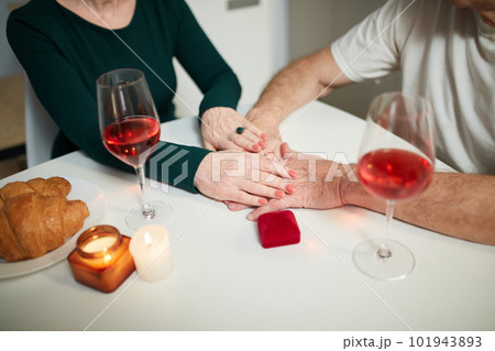 Close-up of couples hands giving support and love. Senior couple having romantic dinner at home in kitchen with wine and presents Close-up of couples hands giving support and love. Senior couple having romantic dinner at home in kitchen with wine and presents 101943893