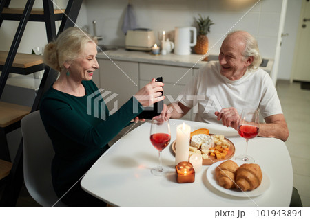 Happy beautiful wife receiving present from her husband. Senior couple having romantic dinner, celebrating at home in kitchen. Surprise Happy beautiful wife receiving present from her husband. Senior couple having romantic dinner, celebrating at home in kitchen. Surprise 101943894