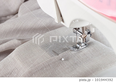 Modern sewing machine presser foot with linen fabric and thread, closeup Modern sewing machine presser foot with linen fabric and thread, closeup 101944392