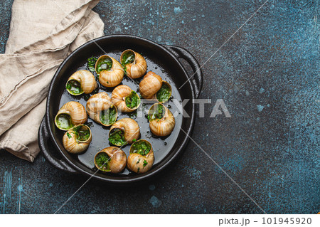 Escargots de Bourgogne Snails with Garlic Butter and Parsley in black cast iron pan on rustic stone background top view, traditional French Delicacy, space for text. Escargots de Bourgogne Snails with Garlic Butter and Parsley in black cast iron pan on rustic stone background top view, traditional French Delicacy, space for text. 101945920