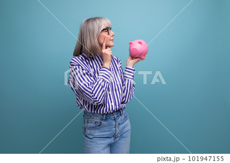 pension contribution. 60s middle aged woman with gray hair holding a piggy bank against a bright 101947155