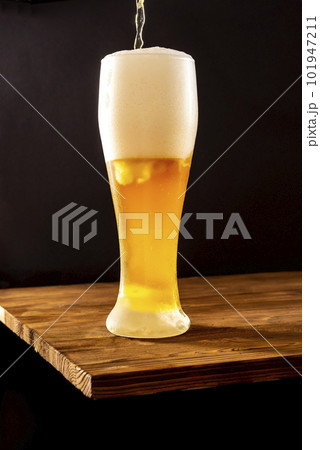 Light craft beer in a misted glass on a wooden table. 101947211