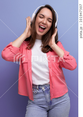 energetic brunette young woman in a shirt and jeans dances to the music from wireless headphones energetic brunette young woman in a shirt and jeans dances to the music from wireless headphones 101947307