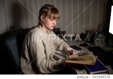 An overworked student sits at night with a book. Make notes in a notebook in the dark. An overworked student sits at night with a book. Make notes in a notebook in the dark. 101948379