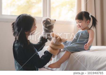Elder asian sister and younger Asian sister playing animal hand puppet doll toys, sitting on bed, Educational preschool games, Having fun with kid at home concept.; 101948785