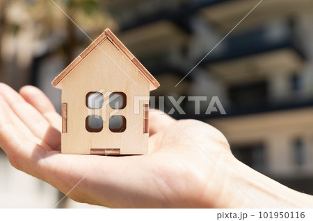 Wooden Model of a country house on a woman's palm with a residential building on the background Wooden Model of a country house on a woman's palm with a residential building on the background 101950116