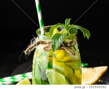 Lemonade in a transparent glass with lemon, lime, rosemary sprigs and mint leaves on a black background Lemonade in a transparent glass with lemon, lime, rosemary sprigs and mint leaves on a black background 101950592