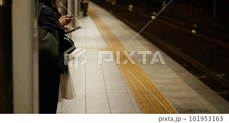 夜の駅のホームでスマホを見ながら電車待ちの女性の姿 101953163