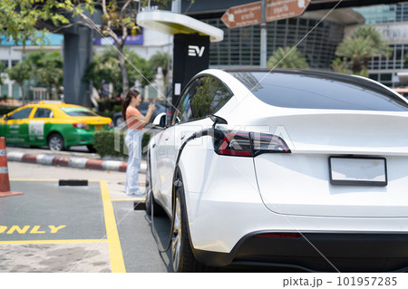 A young woman and her electric car at charging station 101957285