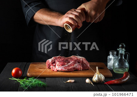 Cook cooking raw meat fillet and adding pepper or chili for marinade on black background. Working environment in kitchen in restaurant or cafe. Cook cooking raw meat fillet and adding pepper or chili for marinade on black background. Working environment in kitchen in restaurant or cafe. 101966471