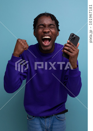 lucky winner african young man with dreadlocks with phone on studio background 101967181