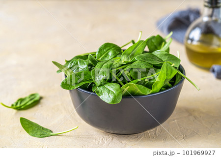 Fresh spinaches in black bowl with olive oil and grey napkin backside on light sand background 101969927