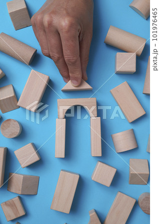 high angle view of a man building a house with some wooden building blocks on a blue background surrounded by some more building blocks 101976465