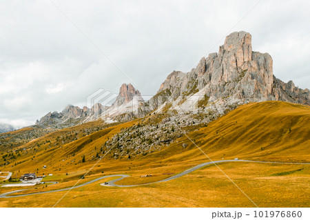 High mountain range near small cottage on Pass Giau slope against evening sky. Rocky cliff with bare peaks illuminated by bright sunset High mountain range near small cottage on Pass Giau slope against evening sky. Rocky cliff with bare peaks illuminated by bright sunset 101976860