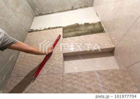Close-up of worker tiler hand with lever installing on walls ceramic tiles. Tiles installation, tools and home improvement, renovation and construction, comfortable modern home concept. Close-up of worker tiler hand with lever installing on walls ceramic tiles. Tiles installation, tools and home improvement, renovation and construction, comfortable modern home concept. 101977704