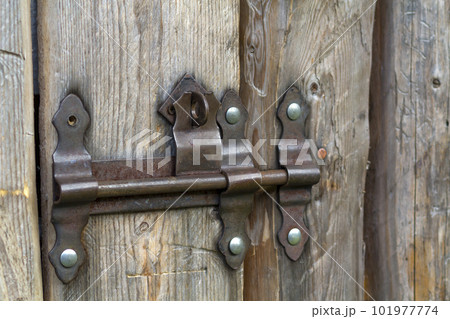 Close-up of lit by sun old rough made of wooden planks house door or barn gate with iron rusty slide bolt lock. Outdated technology, safety, security and protection from thieves concept. 101977774