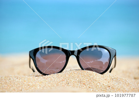 Closeup of black protective sunglasses on sandy beach at tropical seaside on warm sunny day. Summer vacation concept. Closeup of black protective sunglasses on sandy beach at tropical seaside on warm sunny day. Summer vacation concept. 101977787