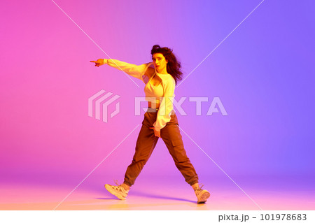 Dynamic image of young sportive girl, female hip-hop dancer training against gradient pink purple background in neon light Dynamic image of young sportive girl, female hip-hop dancer training against gradient pink purple background in neon light 101978683