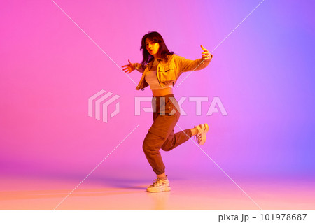 Dynamic image of young female dancer in sport style clothes dancing against gradient pink purple background in neon light 101978687