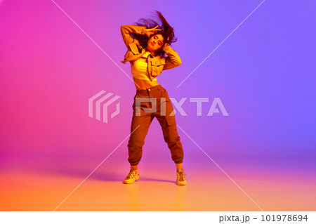 Flexible, artistic young girl, professional dancer in sport clothes dancing hip-hop against gradient pink purple background in neon light 101978694