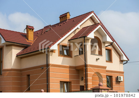 Big modern expensive luxurious residential two-stories cottage, family house with shingled brown roof, high brick chimneys, stucco walls on blue sky copy space background. Real estate selling concept. 101978842