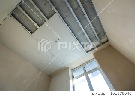 Angled view of light empty room under construction. Suspended ceiling and walls from drywall fixed to metal frame with screws. Renovation, insulation, comfort and do it yourself concept. 101979040