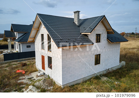 Aerial view of unfinished house with aerated lightweight concrete walls and wooden roof frame covered with metallic tiles under construction Aerial view of unfinished house with aerated lightweight concrete walls and wooden roof frame covered with metallic tiles under construction 101979096