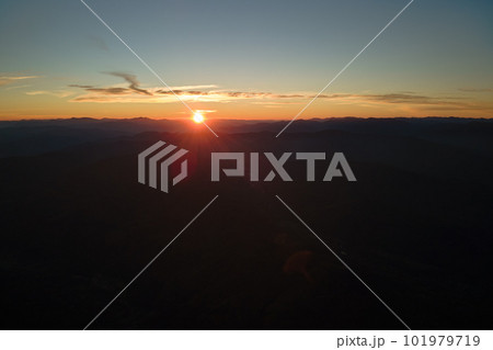 Aerial view of dark mountain hills with bright sunrays of setting sun at sunset. Hazy peaks and misty valleys in evening 101979719