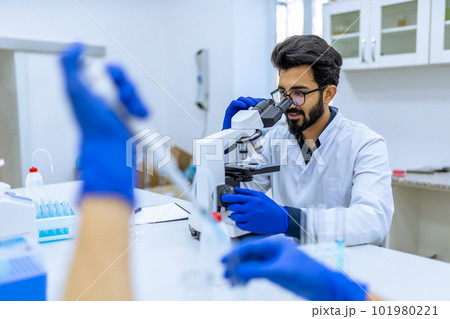 Scientist in glasses reserching microorganisms in microscope, working with unrecognizable colleague Scientist in glasses reserching microorganisms in microscope, working with unrecognizable colleague 101980221