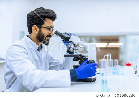 Scientist conducts experiments, adjusts specimen in petri dish and looking on it into microscope 101980230