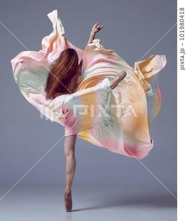 One young adorable ballerina with red hair emotional dancing with over grey studio background. Back view. Elegant colorful dress 101980418