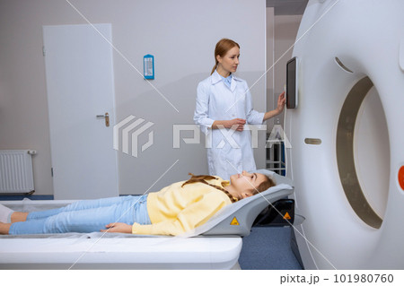 Little girl lying on table of mri scan machine female radiographer pushing button on control panel Little girl lying on table of mri scan machine female radiographer pushing button on control panel 101980760