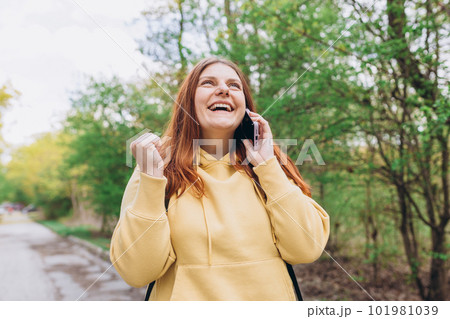 Portrait of a satisfied young woman holding mobile phone and celebrating outdoors. Smiling beautiful women talking on smartphone on nature background Portrait of a satisfied young woman holding mobile phone and celebrating outdoors. Smiling beautiful women talking on smartphone on nature background 101981039